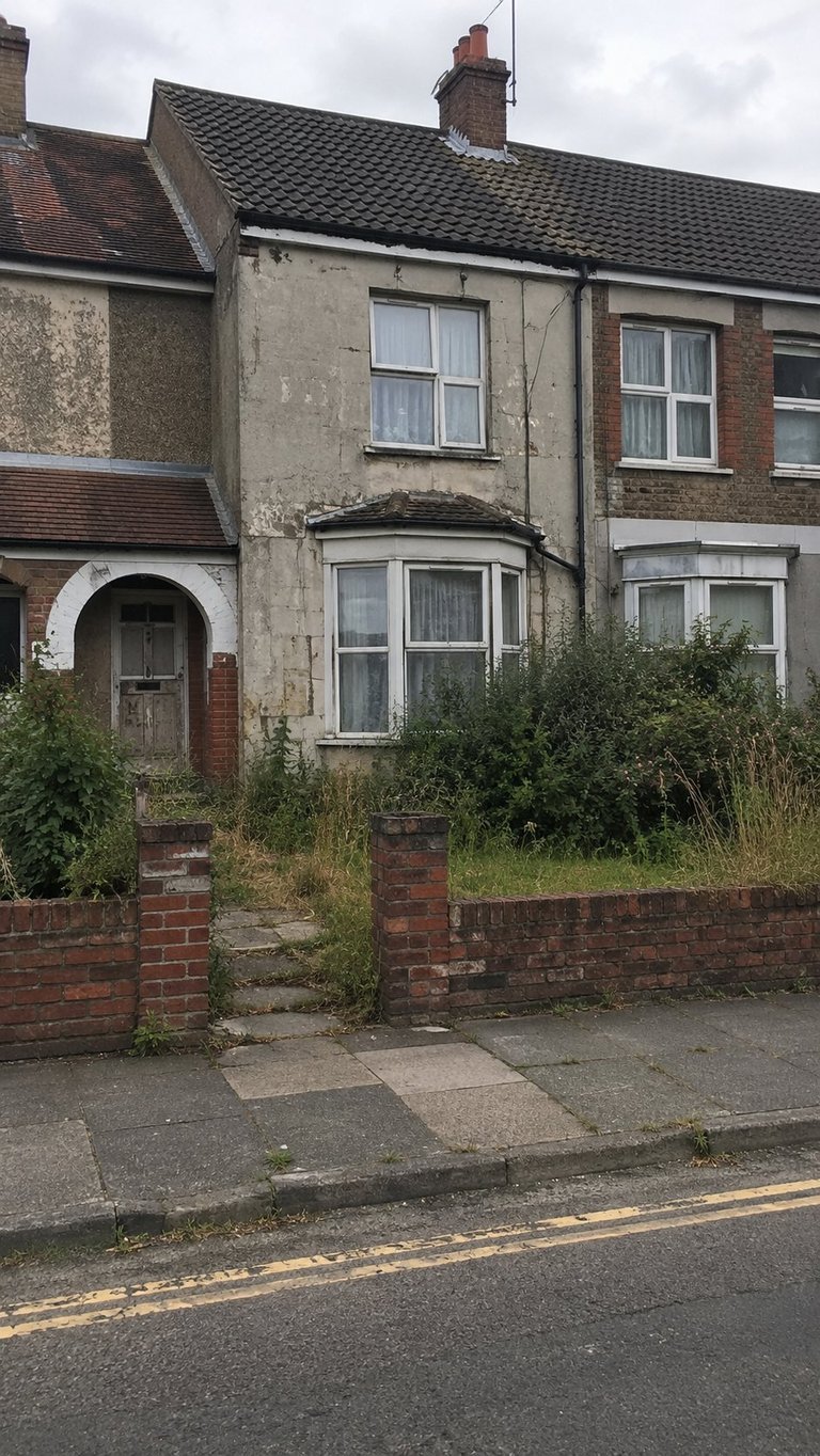 Weathered Victorian townhouse with overgrown vegetation and crumbling facade along brick wall and paved street